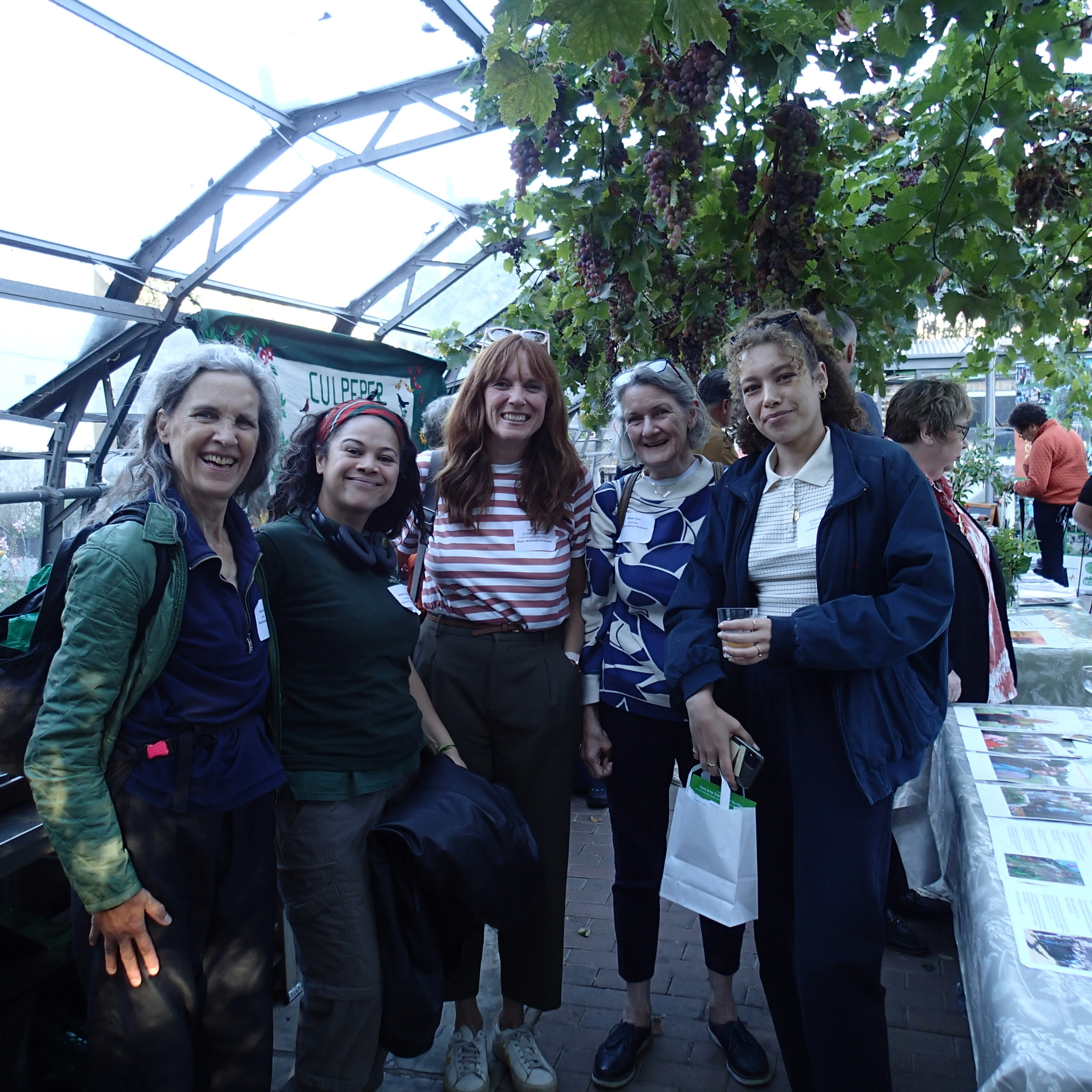 a group of showcase attendees smiling in a glasshouse with grape vines and banners in the background