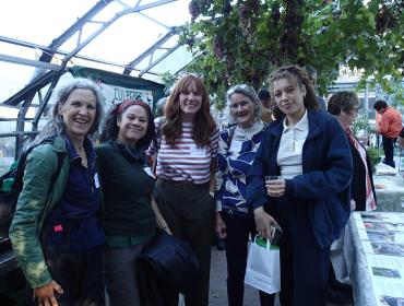 a group of showcase attendees smiling in a glasshouse with grape vines and banners in the background