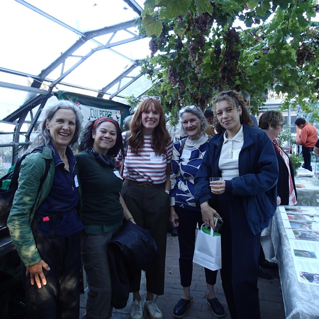 a group of showcase attendees smiling in a glasshouse with grape vines and banners in the background