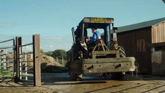 Young person learning to drive a tractor in  a farm yard